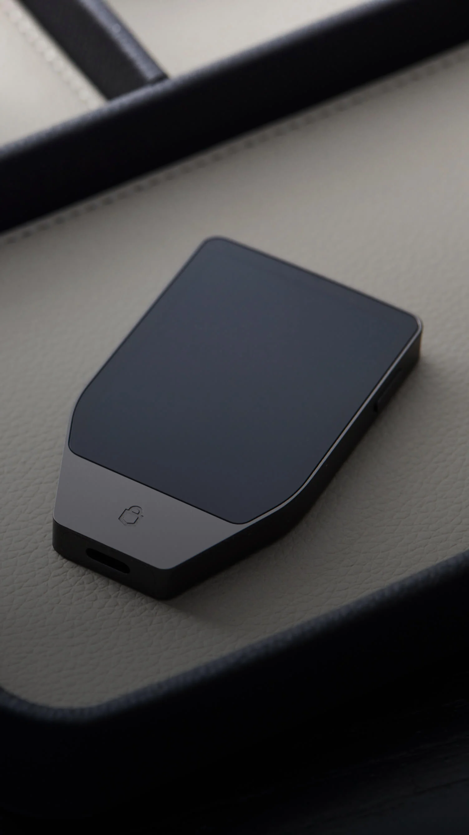 A man sits on a chair using a MacBook while holding a Trezor Safe 7 hardware wallet in one hand.